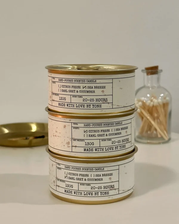 Three stacked Daily Reminder Candle tins showing vintage-inspired labels with scent options displayed