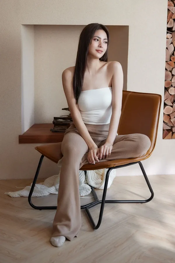 Woman in white thermal strapless bra top with beige pants sitting cross-legged on leather chair near fireplace